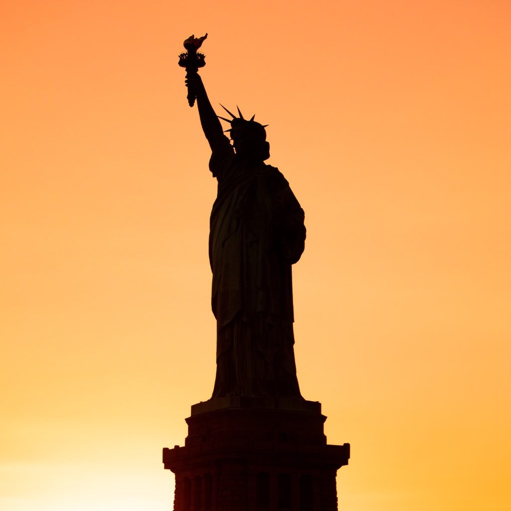 The Statue of Liberty silhouetted against an orange sunset