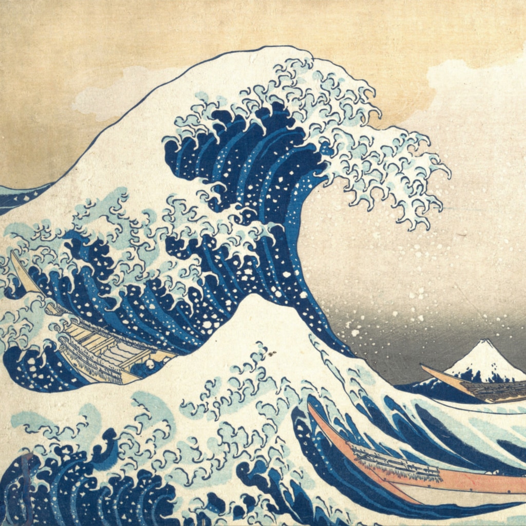 A large blue foamy wave crests as small boats are tossed in the stormy sea with Mount Fuji in the distance