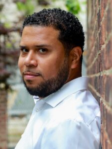 Portrait photograph of bass-baritone Eliam Ramos leaning against a wall.
